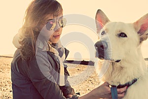 Hipster girl playing with dog at a beach during sunset, strong lens flare