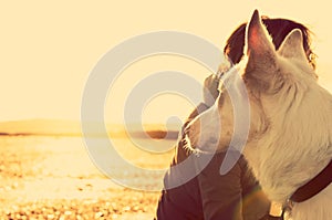 Hipster girl playing with dog at a beach during sunset, strong lens flare effect