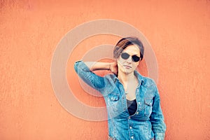 Hipster girl posing, against orange background on city streets. Urban lifestyle of contemporary world