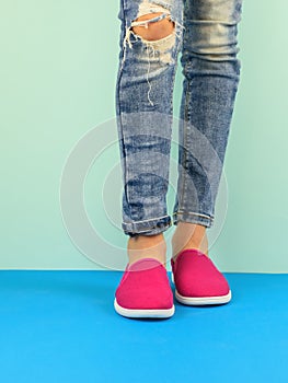 Hipster girl`s legs in ripped jeans on the blue floor by the blue wall. Modern style.