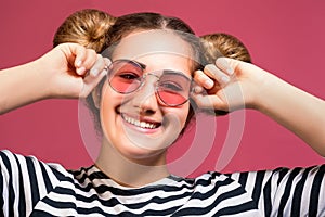 Hipster girl in sunglasses and striped shirt with playful hairstyle isolated over pink background