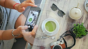 Hipster Girl Taking Photo of Matcha Green Tea Latte in Cup. Beautiful Lifestyle Table Composition in Cafe. HD Slowmotion