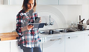 Hipster girl using tablet technology and drink coffee in kitchen, girl person holding computer on background interior cuisine, fem