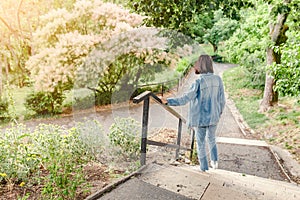 Girl walks along the path in the city park and looking at the blooming trees at spring time