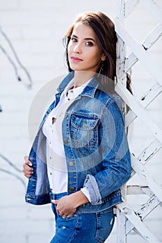 Hipster girl wearing blank white shirt, jeans and jeans jacket posing against street wall. Minimalist urban clothing