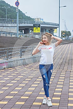 Hipster girl wearing blank white t-shirt, jeans and baseball cap posing against rough street wall, full length portrait,