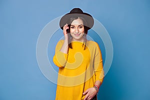 Hipster girl wearing stylish hat and yellow sweater on blue