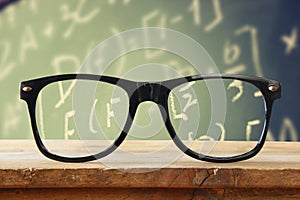 Hipster glasses on a wooden rustic table in front blackboard with math formulas and calculation. vintage filtered