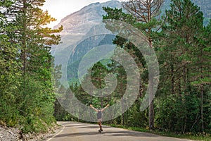 Hipster guy with long board with open arms enjoying life in the middle of a mountain road and a beautiful landscape.