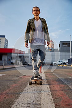 Hipster guy riding skateboard prefers eco-friendly transportation among city