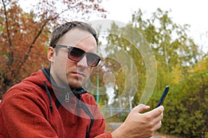 Hipster guy using smartphone device outdoor, outdoor portrait of young cheerful man texting an sms message at social networks, tec