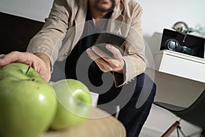 hipster hand using smart phone for mobile payments online business,sitting on sofa in living room,holding green apple in wooden t