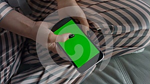 Hipster hands scrolling green smartphone screen closeup. Girl resting on sofa