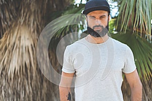 Hipster handsome male model with beard wearing gray blank t-shirt and a black snapback cap with space for your logo or