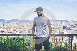 Hipster handsome male model with beard wearing gray blank t-shirt and a black snapback cap with space for your logo or