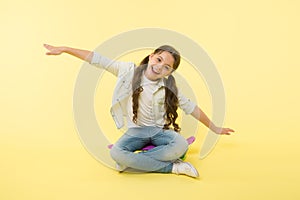 Hipster happy child pretend flying on penny board on yellow background. Little girl dream of sky with arms outstretched