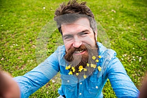 Hipster on happy face taking selfie photo. Man with beard enjoys spring, green meadow background, defocused. Natural