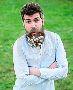 Hipster on happy surprised face stand on grass, defocused. Natural beauty concept. Guy looks nicely with daisy flowers