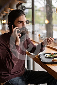 Hipster having lunch in a cafe or fast food restaurant, food on a tray, healthy eating, diet, calling on the phone