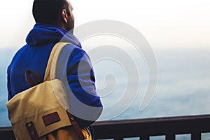 Hipster hiker tourist with backpack looking of amazing seascape sunset on background blue sea, guy enjoying ocean horizon