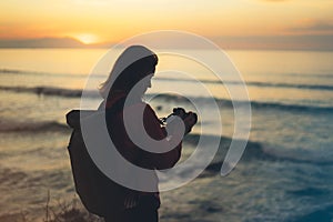Hipster hiker tourist with backpack taking photo of amazing seascape sunset on camera on background blue sea, photographer enjoy