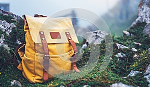 Hipster hiker tourist yellow backpack on background green grass nature in mountain, blurred panoramic landscape, traveler relax