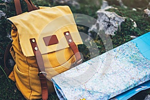 Hipster hiker tourist yellow backpack closeup and navigation map europe on background green grass nature, blurred panoramic landsc