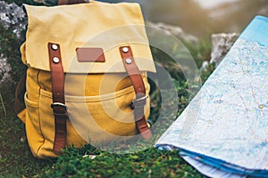 Hipster hiker tourist yellow backpack closeup and navigation map europe on background green grass nature, blurred panoramic landsc