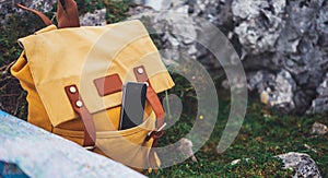 Hipster hiker tourist yellow backpack and mobile phone, map on background green grass nature in mountain, blurred panoramic land