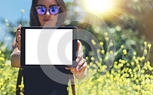 Hipster holding in hands tablet computer. Girl traveler with sunglasses using gadget on sun flare and yellow flowers background