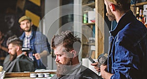 Hipster lifestyle concept. Barber with hairdryer works on hairstyle for bearded man barbershop background. Hipster