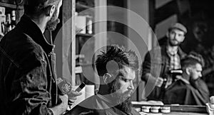 Hipster lifestyle concept. Barber with hairdryer works on hairstyle for bearded man barbershop background. Hipster