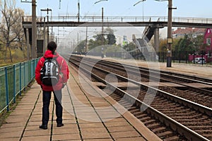 Hipster Man with backpack waiting for a train on railway platform
