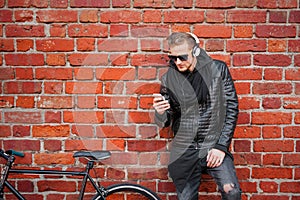 Hipster man with bicycle standing by the brick wall and listening to music