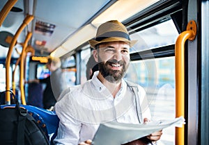 Hipster man on a bus in the city, travelling to work and reading newspapers.