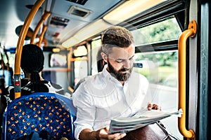 Hipster man on a bus in the city, travelling to work and reading newspapers.