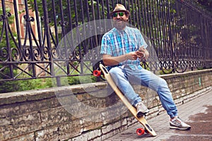 Hipster man chatting at the park with long board. Handsome men in sunglasses and hat posing outdoor