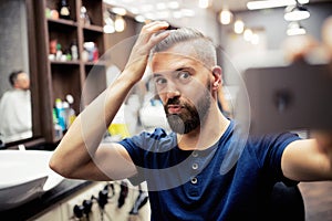 Hipster man client in barber shop, making funny faces when taking seflie.