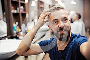 Hipster man client in barber shop, taking seflie.