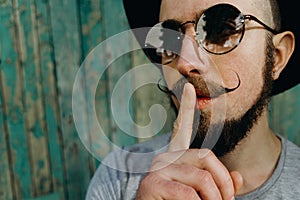 Hipster man gesture for silence showing hush sign