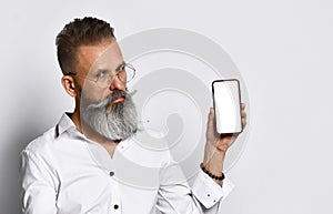 Hipster man with glasses shows the phone to the camera and confidently smiling.