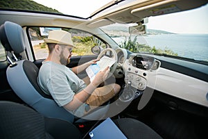 Hipster man looking on location navigation map in car, tourist traveler driving and hold in male hands europe