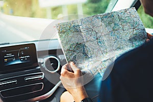 Hipster man looking and point finger on location navigation map in car, tourist traveler driving and hold in male hands europe car