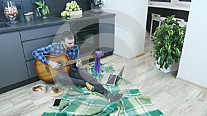 Hipster man play acoustic guitar sitting on floor at home. Young musician practicing playing guitar staying at home during selfiso