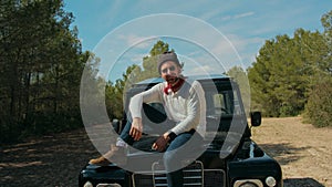 Hipster man sits on black adventure jeep in forest