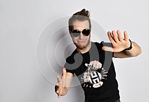 Hipster man in sunglasses, black t-shirt with print, bracelets. He smiling and gesticulating, posing isolated on white. Close up