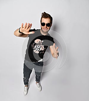 Hipster man in sunglasses, black t-shirt with print, bracelets. He smiling and gesticulating, posing isolated on white. Close up