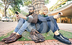 Hipster millennial couple in disinterest moment with smartphone - Apathy concept about sadness and isolation using mobile phone photo