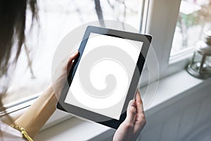 Hipster person hands holding digital tablet with empty blank screen, against a background of window horizontal, freelancer girl