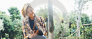 Hipster person holding in hands digital tablet with screen, young girl smile reading on computer on background nature park palm